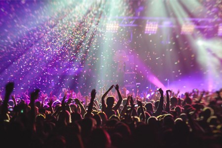 Stor publik framför en scen med armarna uppsträckta i ljuset av strålkastare och nedsignande konfetti