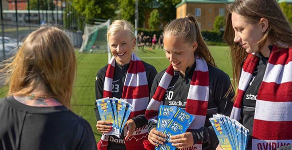 Tre kvinnor i fotbollsställ säljer bingolotter och sverigelotter ute i solen