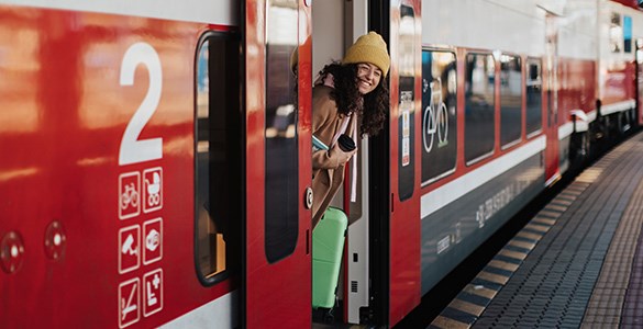 En kvinna vinkar glatt ut genom dörren på ett tåg som står vid perrongen