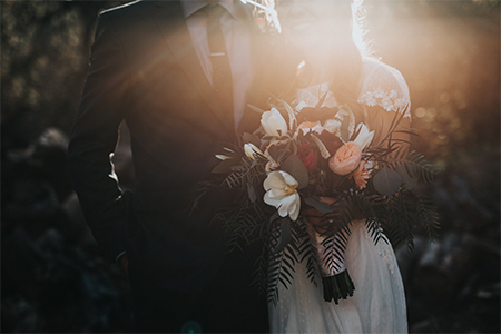 Bröllopspar i kostym och brudklänning hållandes i en stor blombukett 